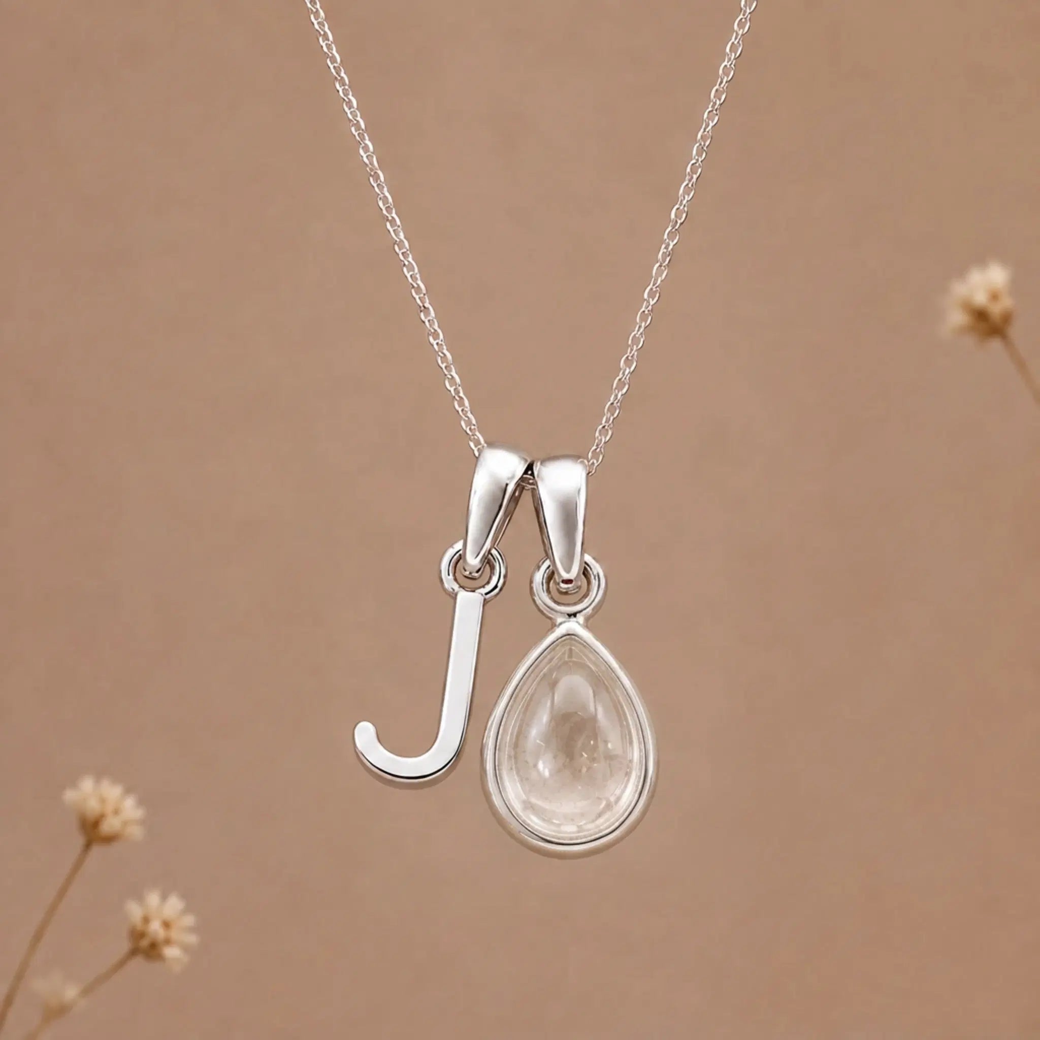 sterling silver initial j april birthstone natural clear quartz pendant necklace against a dark warm beige background