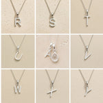 Collection of silver letter necklaces R to Z on a beige background as initial options for a personalised April Birthstone Clear Quartz Necklace.
