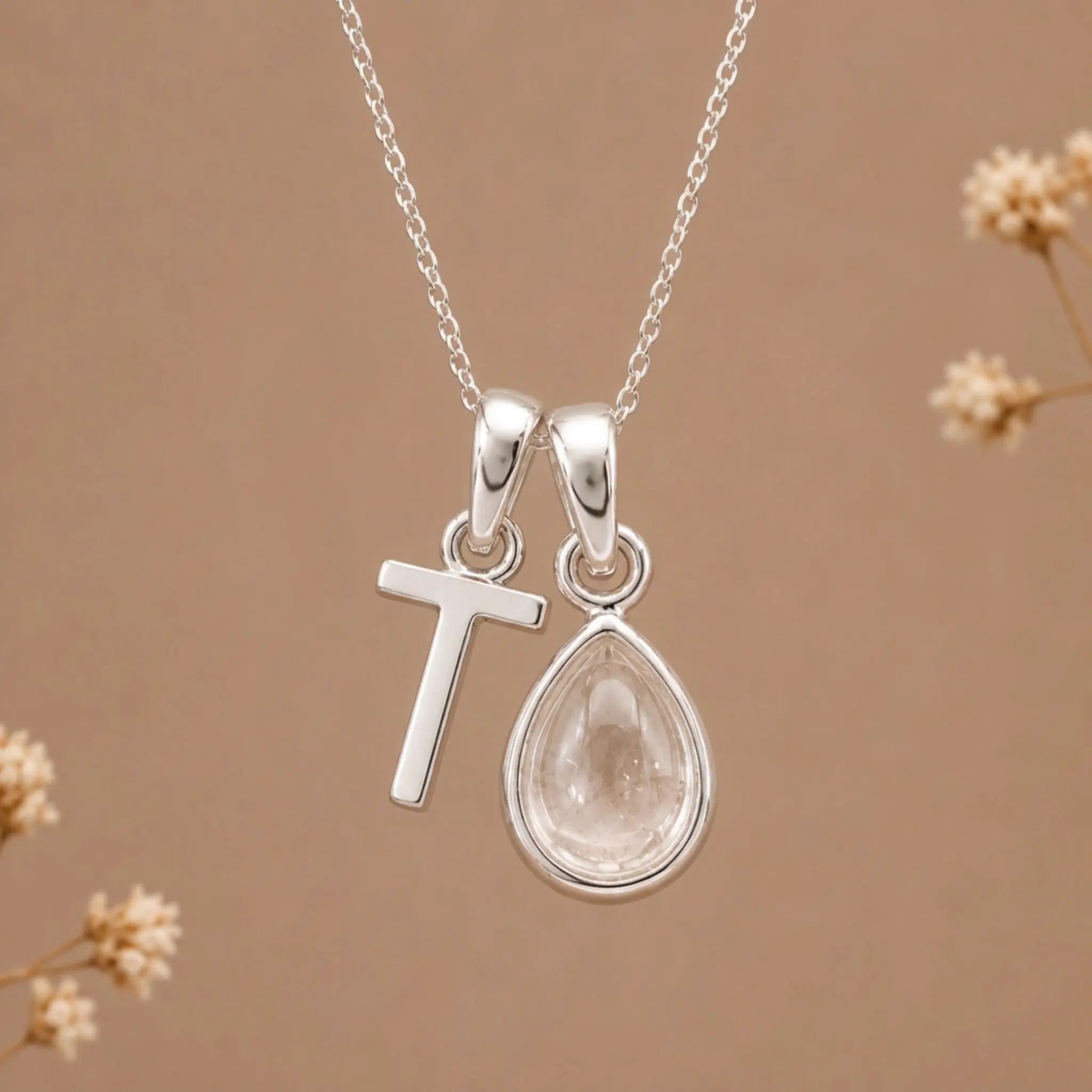 sterling silver initial t april birthstone natural clear quartz pendant necklace against a dark warm beige background