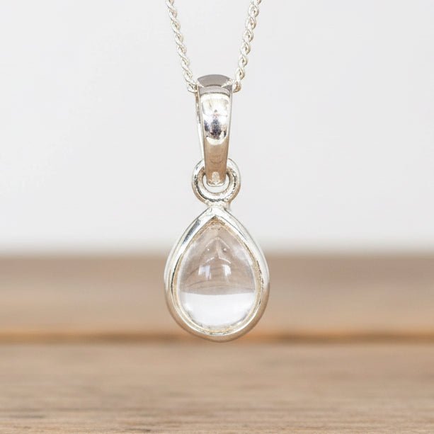 Teardrop-shaped pendant with a clear stone on a chain against a neutral background