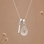 sterling silver initial i april birthstone natural clear quartz pendant necklace against a dark warm beige background