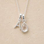 sterling Silver double pendant necklace with a teardrop april birthstone clear quartz pendant and letter 'A' charm on a beige background