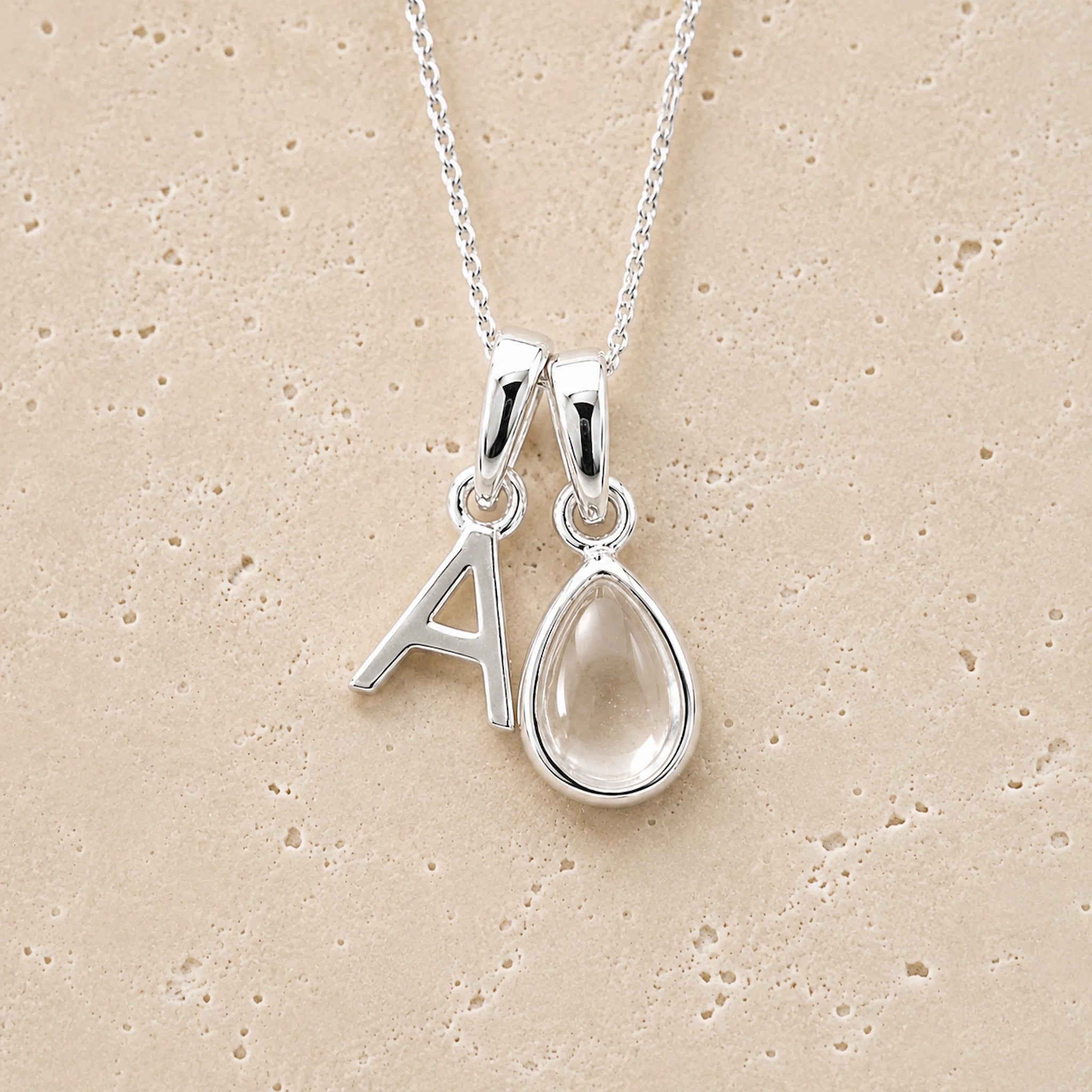 sterling Silver double pendant necklace with a teardrop april birthstone clear quartz pendant and letter 'A' charm on a beige background
