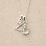 Silver necklace with 'Z' pendant and teardrop-shaped april birthstone clear quartz stone on beige background