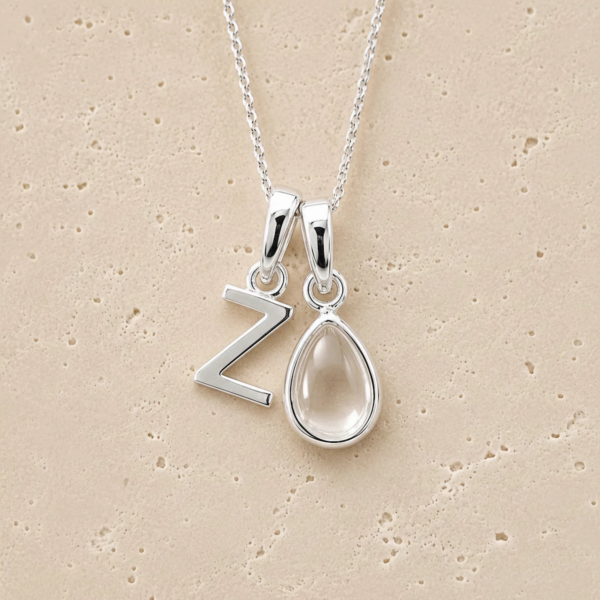 Silver necklace with 'Z' pendant and teardrop-shaped april birthstone clear quartz stone on beige background