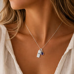 Sterling Silver necklace with a teardrop february birthstone natural amethyst pendant and engraved aquarius glyph tag on person wearing a white shirt.