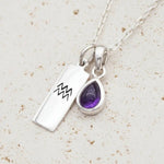 Silver Aquarius zodiac pendant and february Birthstone amethyst pendant on a Sterling Silver Necklace on a stone surface