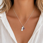 Sterling Silver necklace with a teardrop january birthstone natural garnet pendant and engraved aquarius glyph tag on a model with wearing a white shirt.