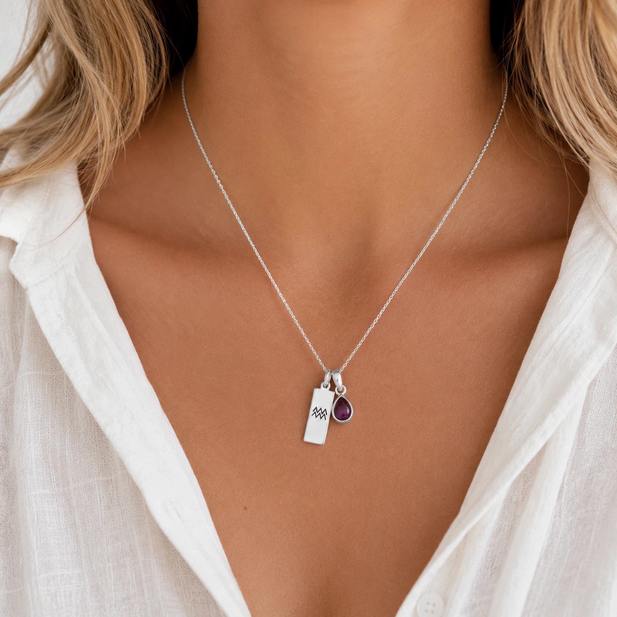 Sterling Silver necklace with a teardrop january birthstone natural garnet pendant and engraved aquarius glyph tag on a model with wearing a white shirt.