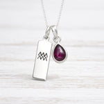 Silver necklace with a pendant featuring a gemstone on a light wooden background