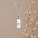 aquarius necklace - A silver rectangular pendant necklace with a black engraved aquarius star sign line glyph symbol, hanging from a delicate silver chain against a warm beige background 