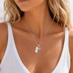 sterling silver necklace with march birthstone aquamarine pendant and rectangle pendant with engraved aries line glyph on a person wearing a white singlet