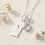Sterling silver necklace with march birthstone aquamarine pendant and rectangle pendant with engraved aries line glyph on a light background.