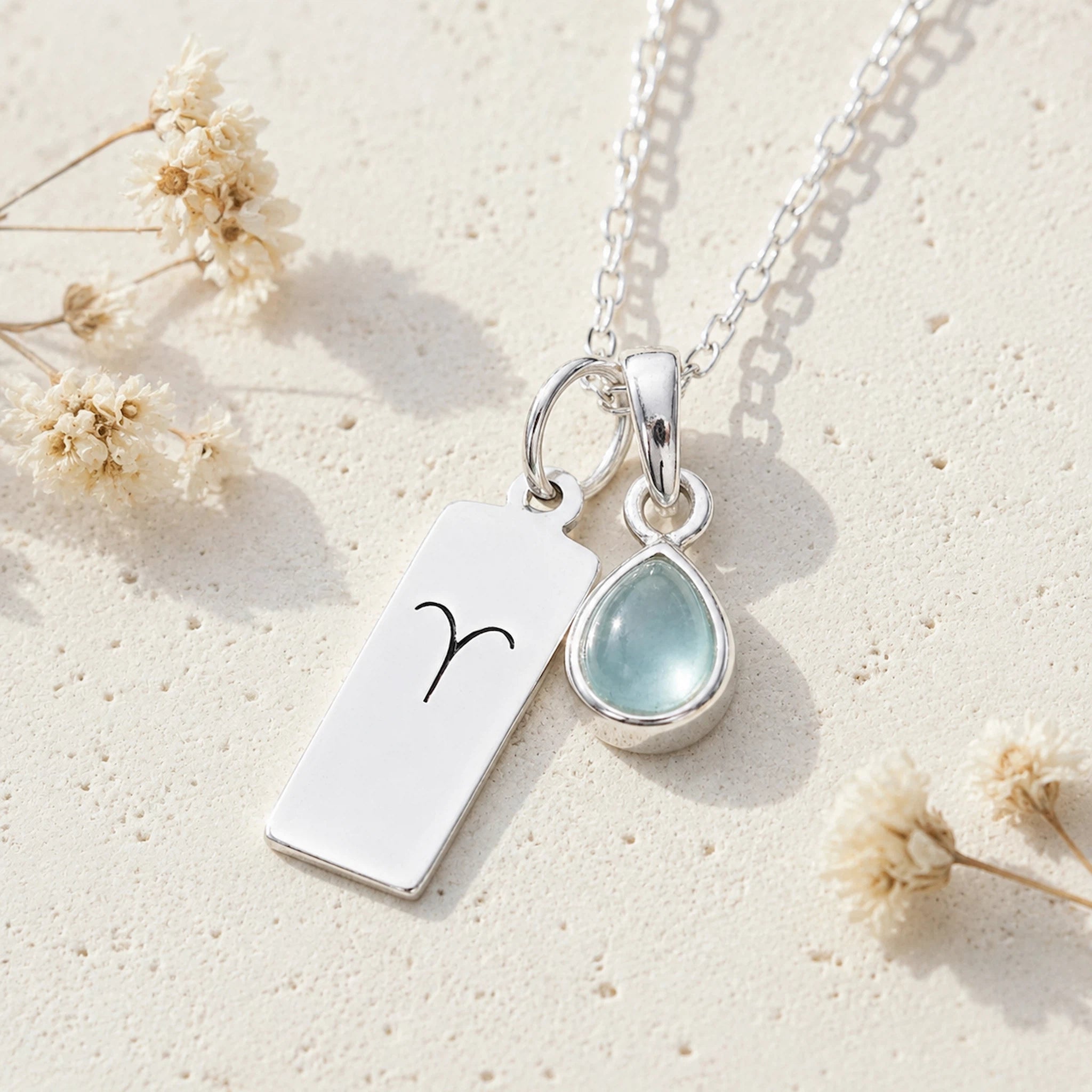 Sterling silver necklace with march birthstone aquamarine pendant and rectangle pendant with engraved aries line glyph on a light background.
