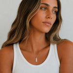 A woman with long highlighted brown hair wearing a silver rectangular pendant necklace engraved with Aries zodiac line glyph