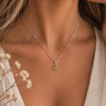 A close-up of a woman's neck and chest wearing a august birthstone necklace featuring a delicate silver chain necklace with a small teardrop-shaped green peridot gemstone pendant