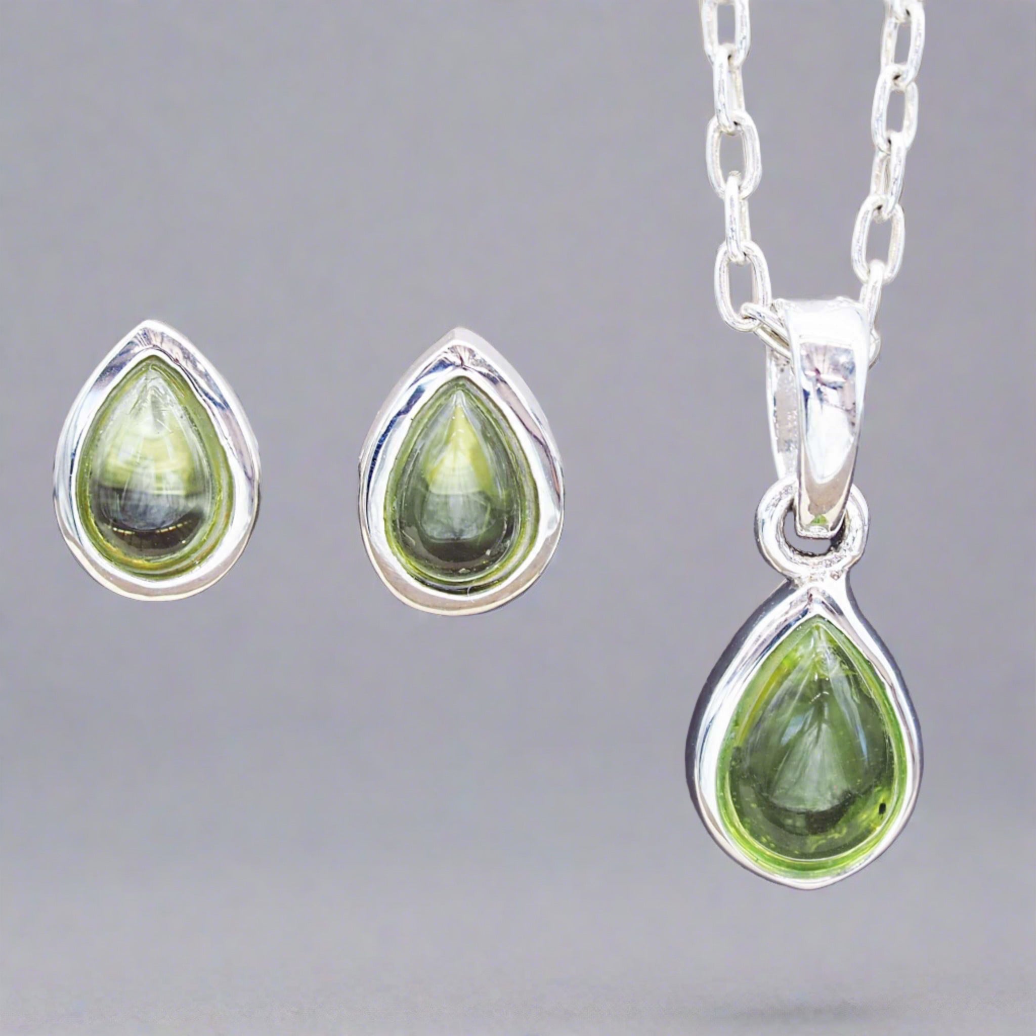 Sterling silver August birthstone Peridot jewellery set featuring tear drop natural peridot stud earrings and matching necklace on a stone surface