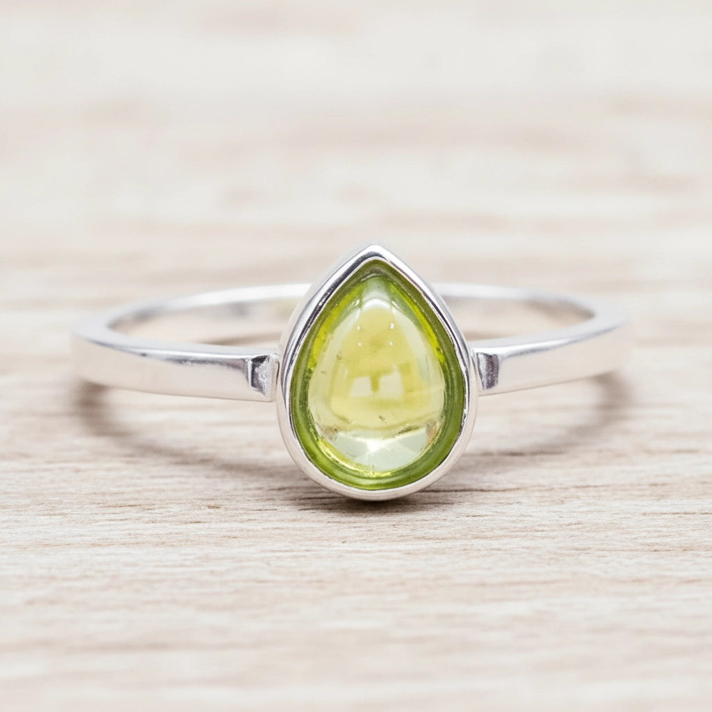 Silver ring with a green peridot teardrop-shaped gemstone on a wooden surface