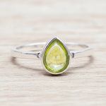 Silver ring with a green peridot teardrop-shaped gemstone on a wooden surface