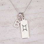 Sterling silver Gemini initial necklace with a letter B and engraved zodiac bar on light wood