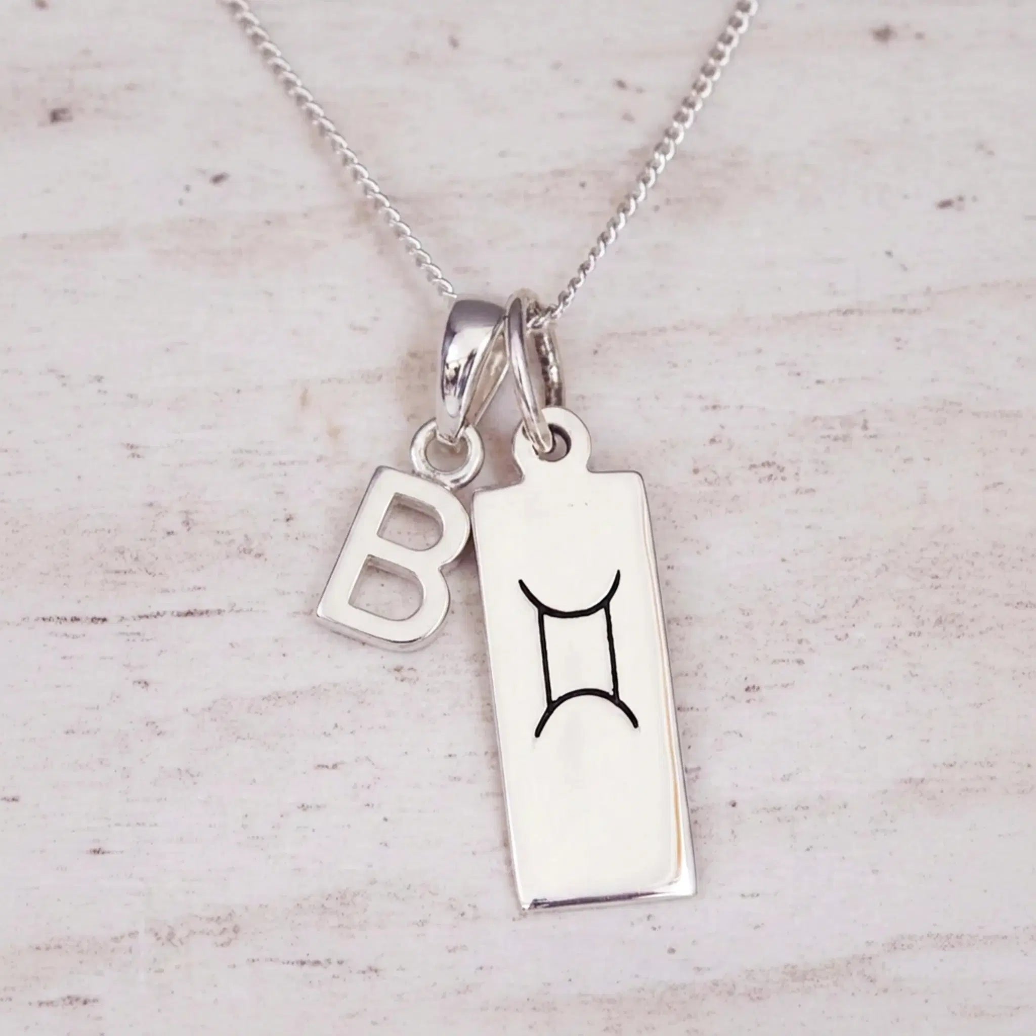 Sterling silver Gemini initial necklace with a letter B and engraved zodiac bar on light wood