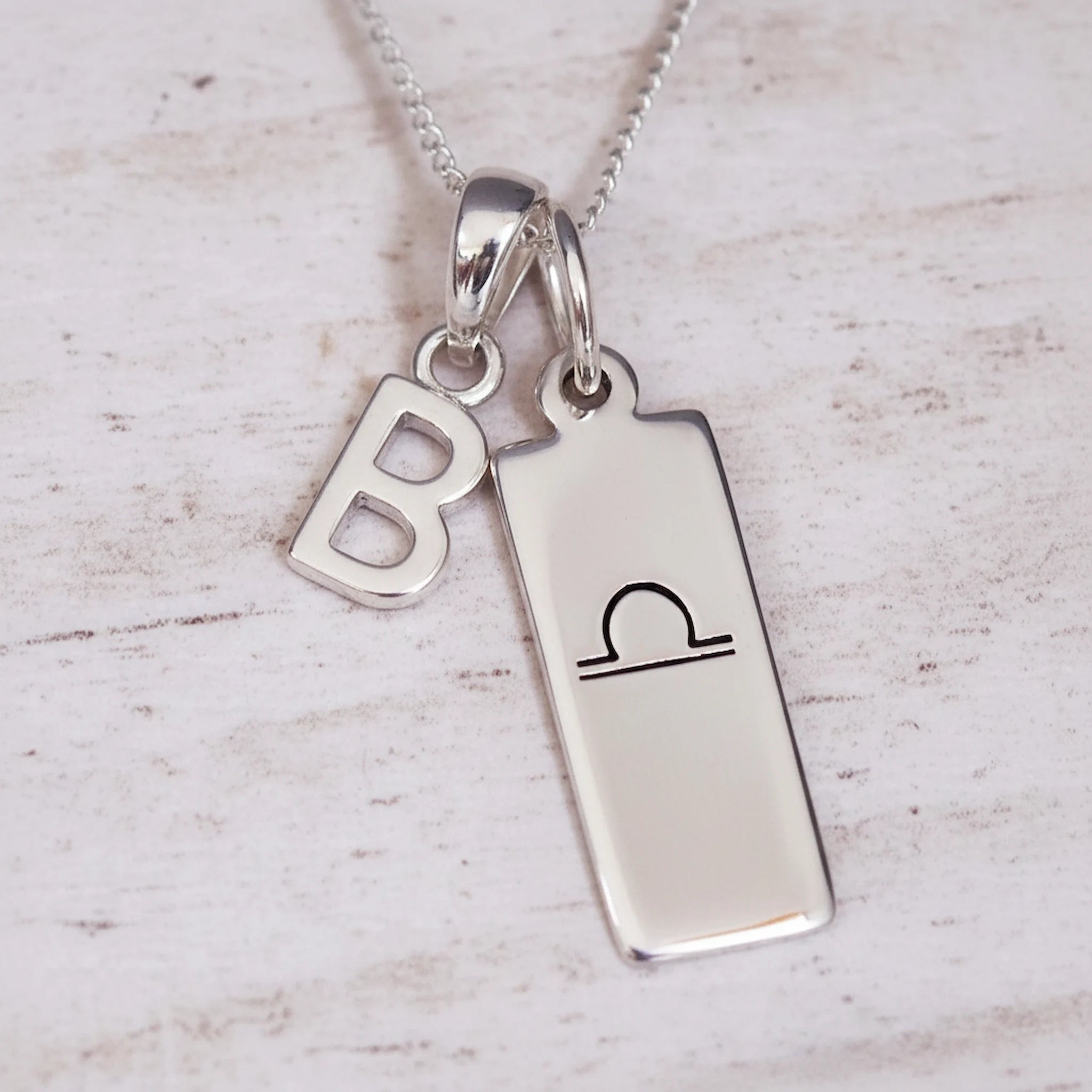 sterling Silver necklace with a libra zodiac pendant and a 'B' initial pendant on a light wooden background
