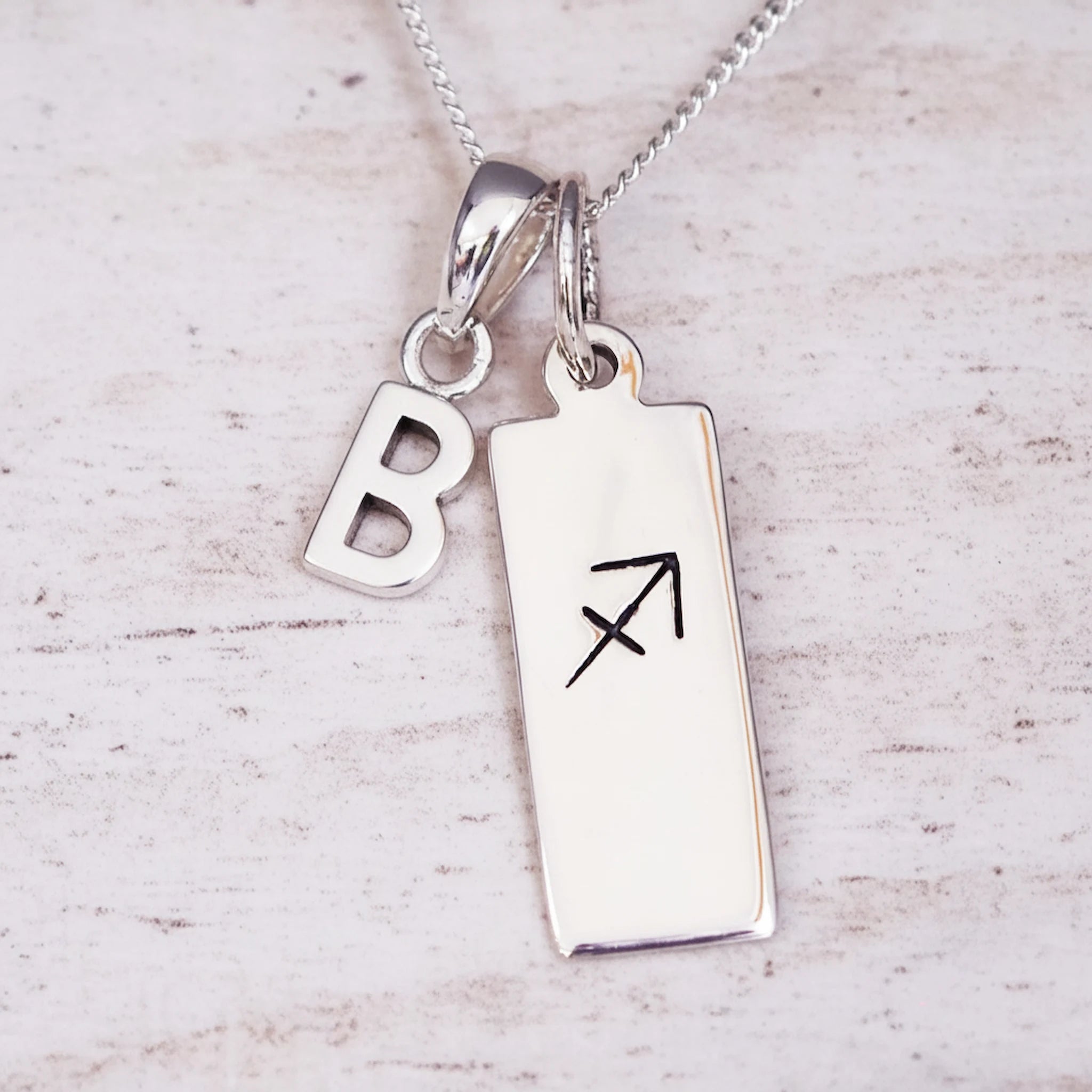 sterling silver necklace with a 'B' initial pendant and a sagittarius zodiac pendant on a light background