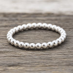 A silver beaded band ring resting on a rustic, weathered wood surface.