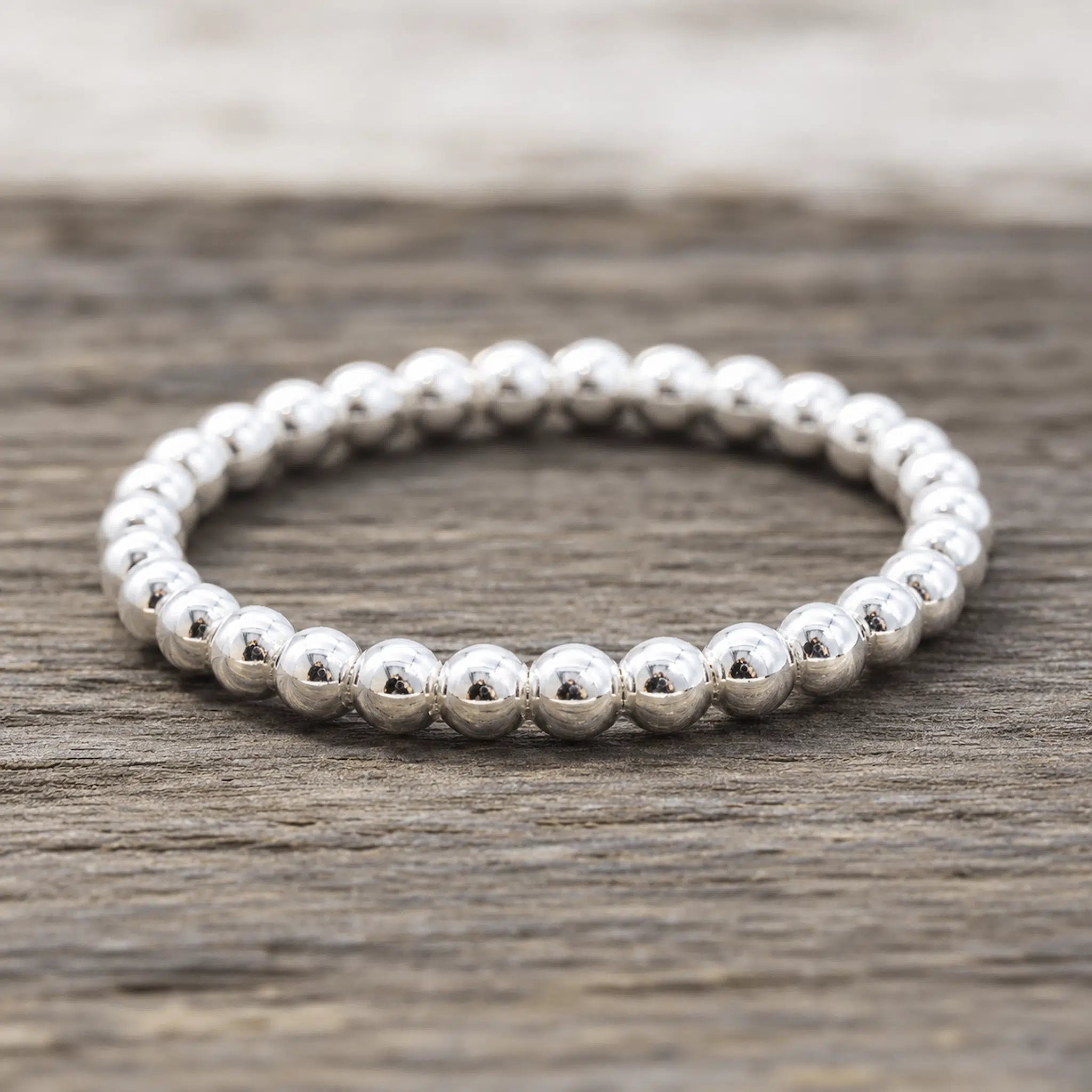 A silver beaded band ring resting on a rustic, weathered wood surface.