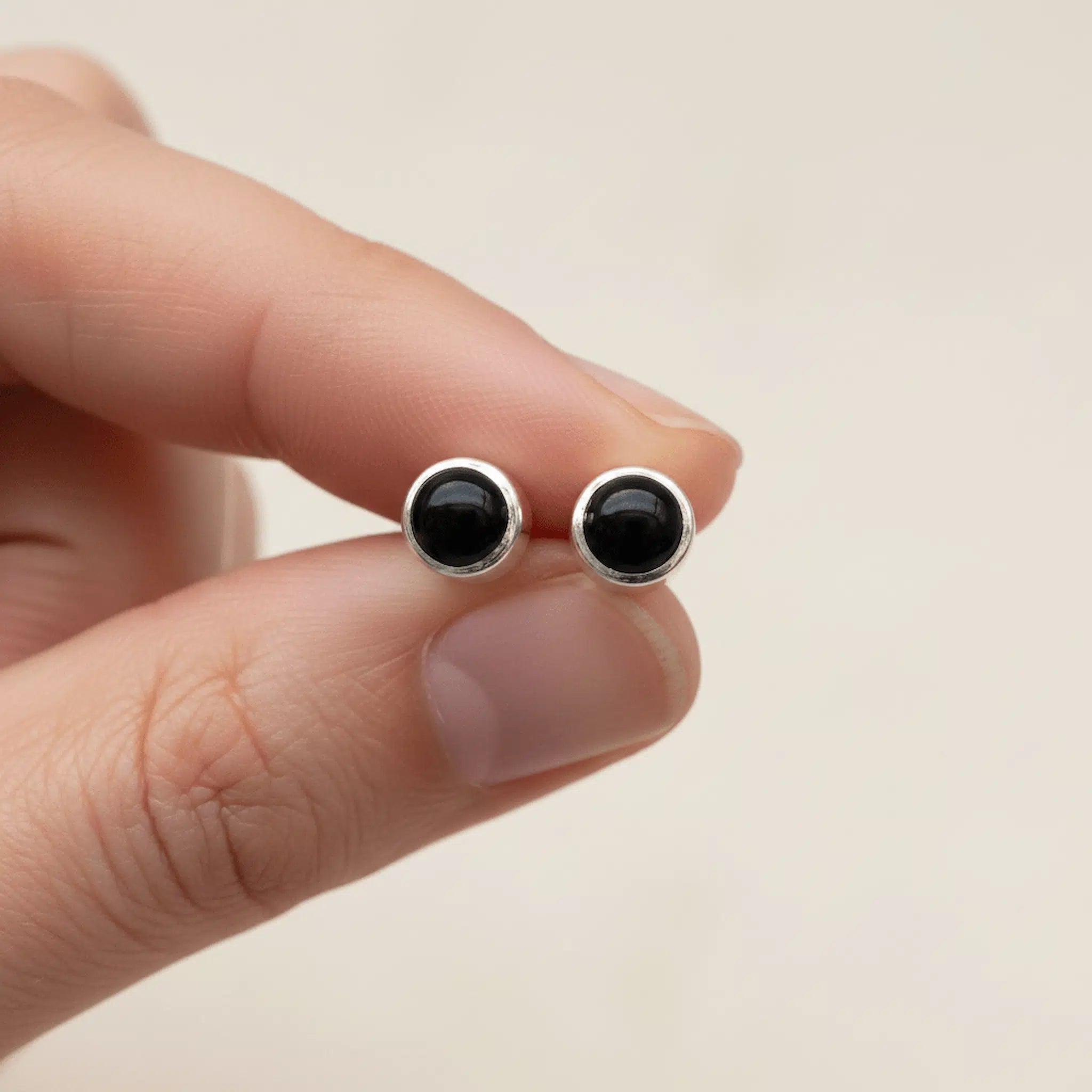 sterling silver round Black onyx stud earrings held between fingers against a neutral background