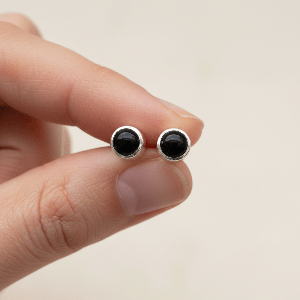 Black onyx stud earrings held between fingers against a neutral background