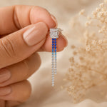 Earring with blue and clear gemstones held by a hand against a blurred natural background
