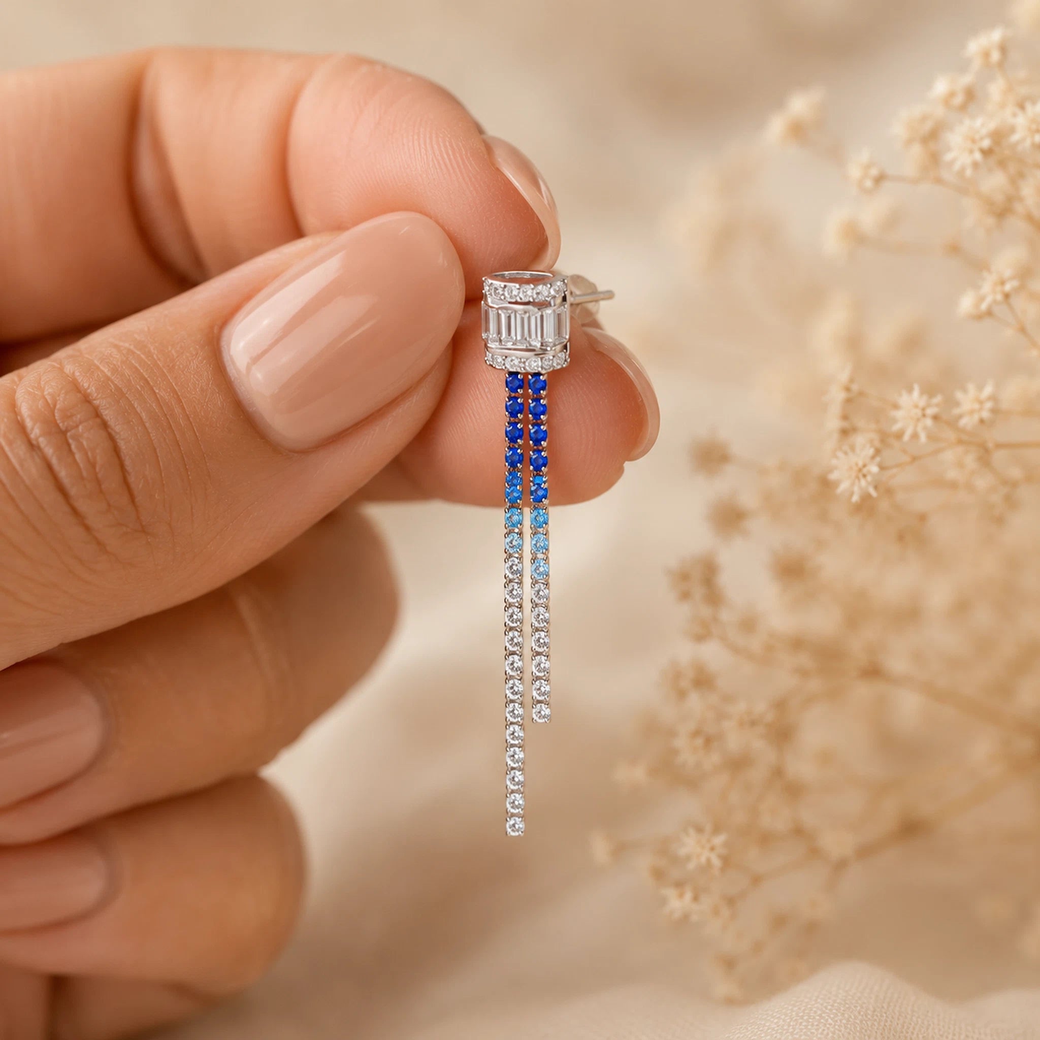 Earring with blue and clear gemstones held by a hand against a blurred natural background