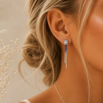 Close-up of a woman wearing blue and silver earrings with a neutral background