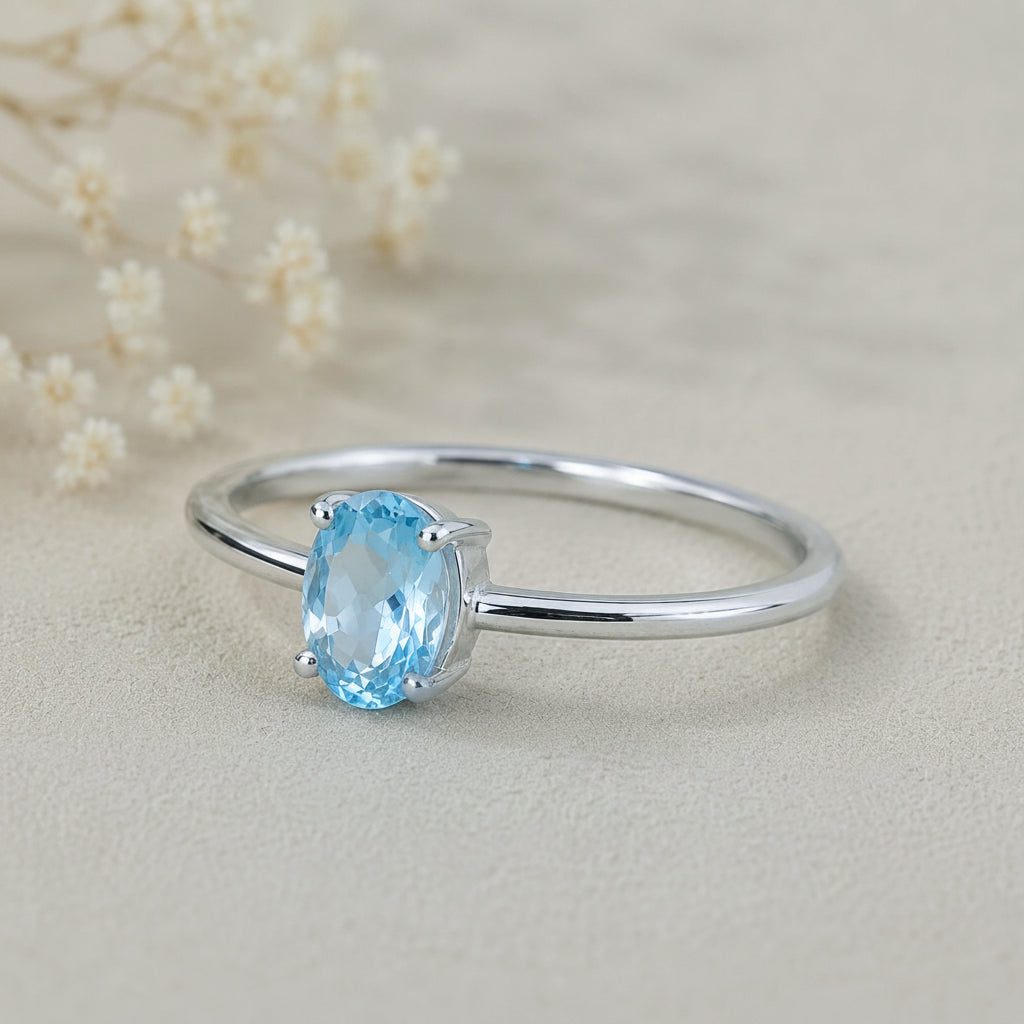 sterling silver ring with a oval shaped faceted claw set blue topaz gemstone on a light surface.