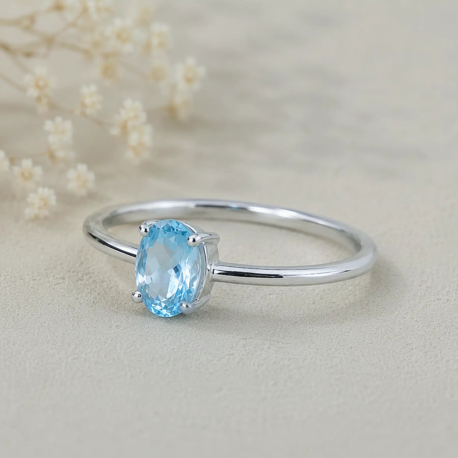 sterling silver ring with a oval shaped faceted claw set blue topaz gemstone on a light surface.