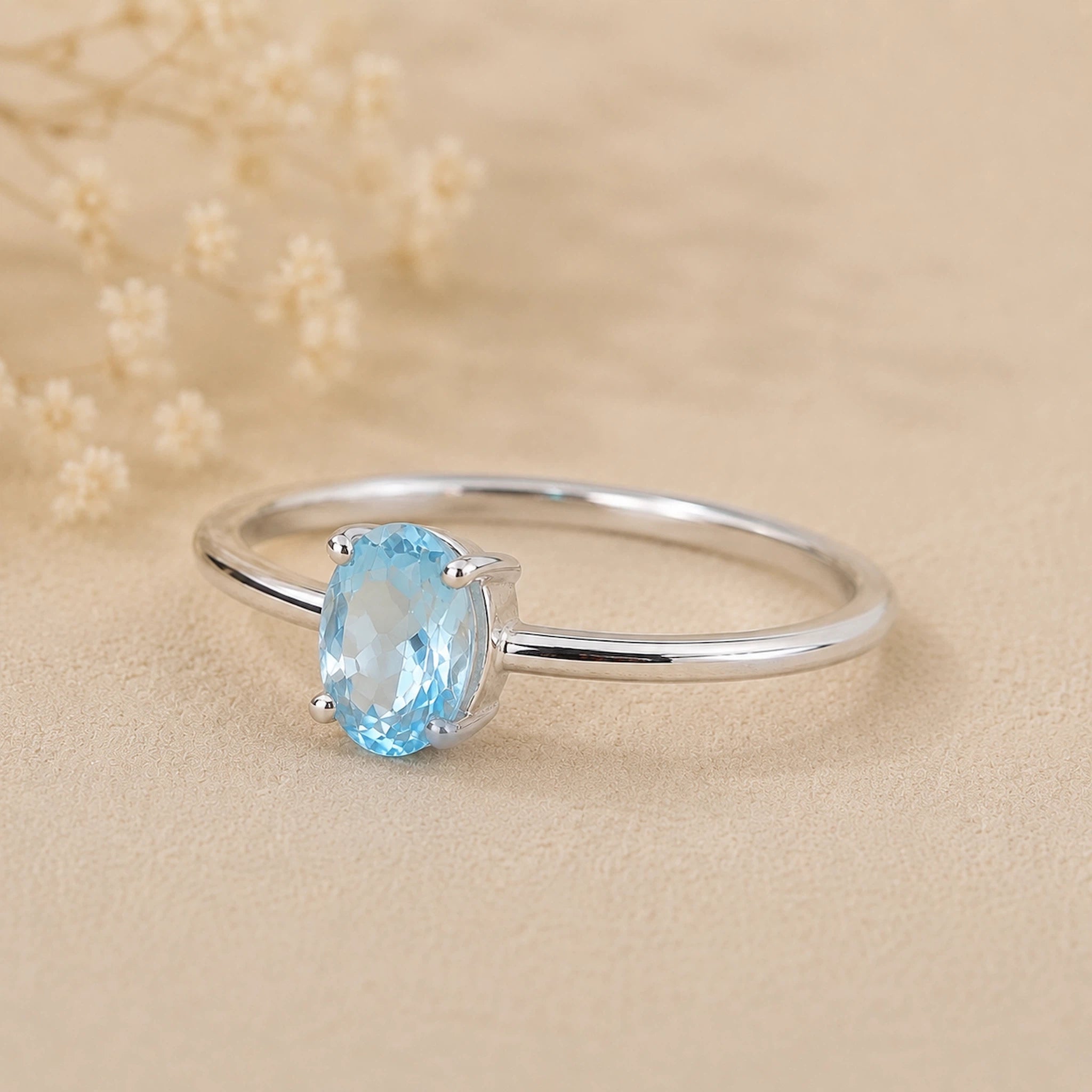 sterling silver ring with a oval shaped faceted claw set blue topaz gemstone on a light surface.