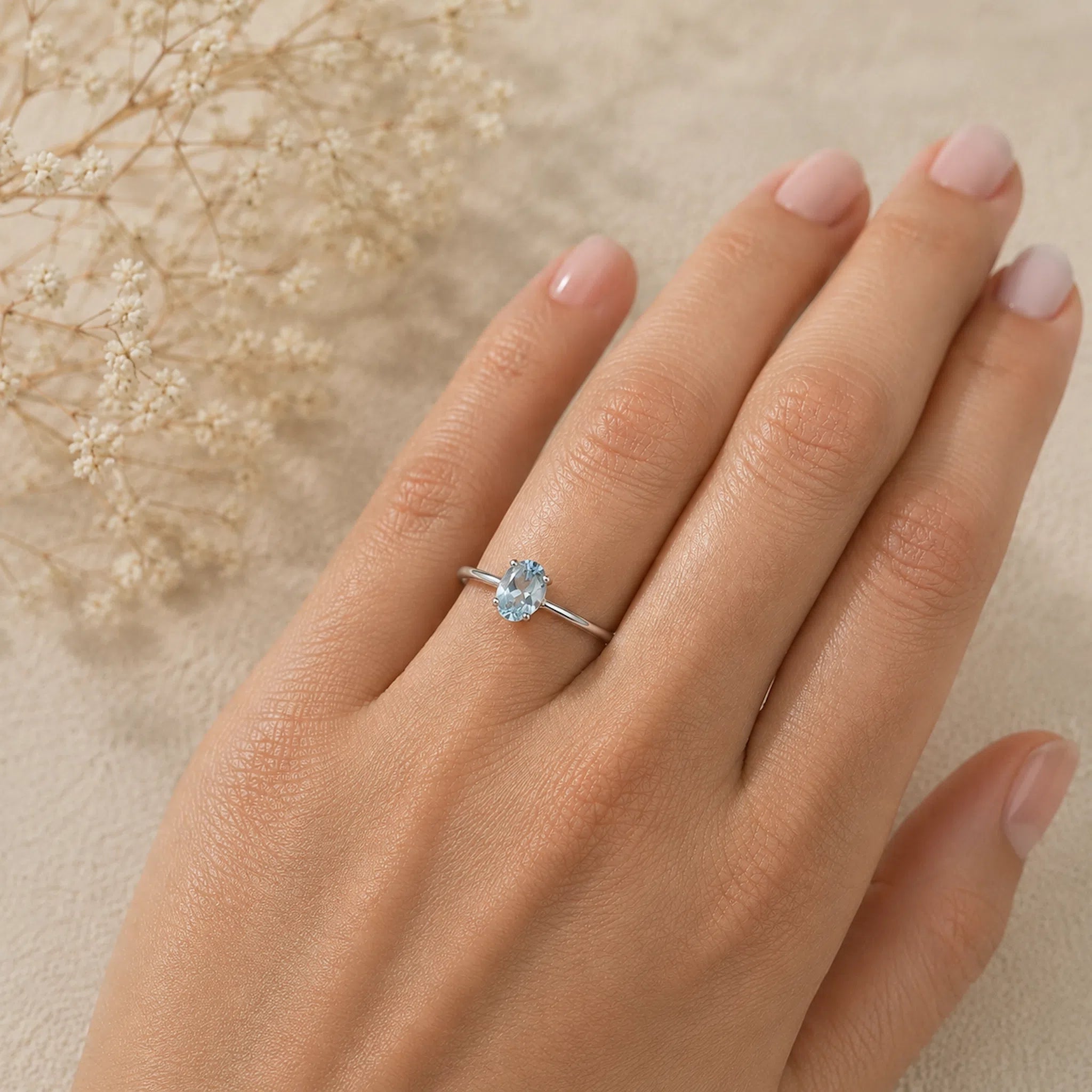 hand wearing a sterling silver ring with a oval shaped faceted claw set blue topaz gemstone with a light background.