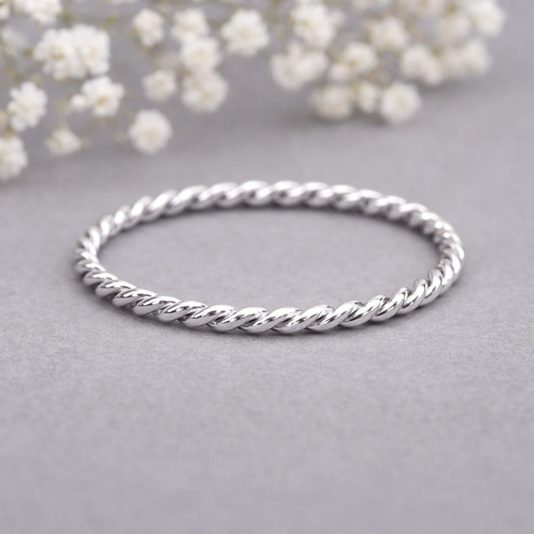 Silver twist ring on a gray surface with white flowers in the background