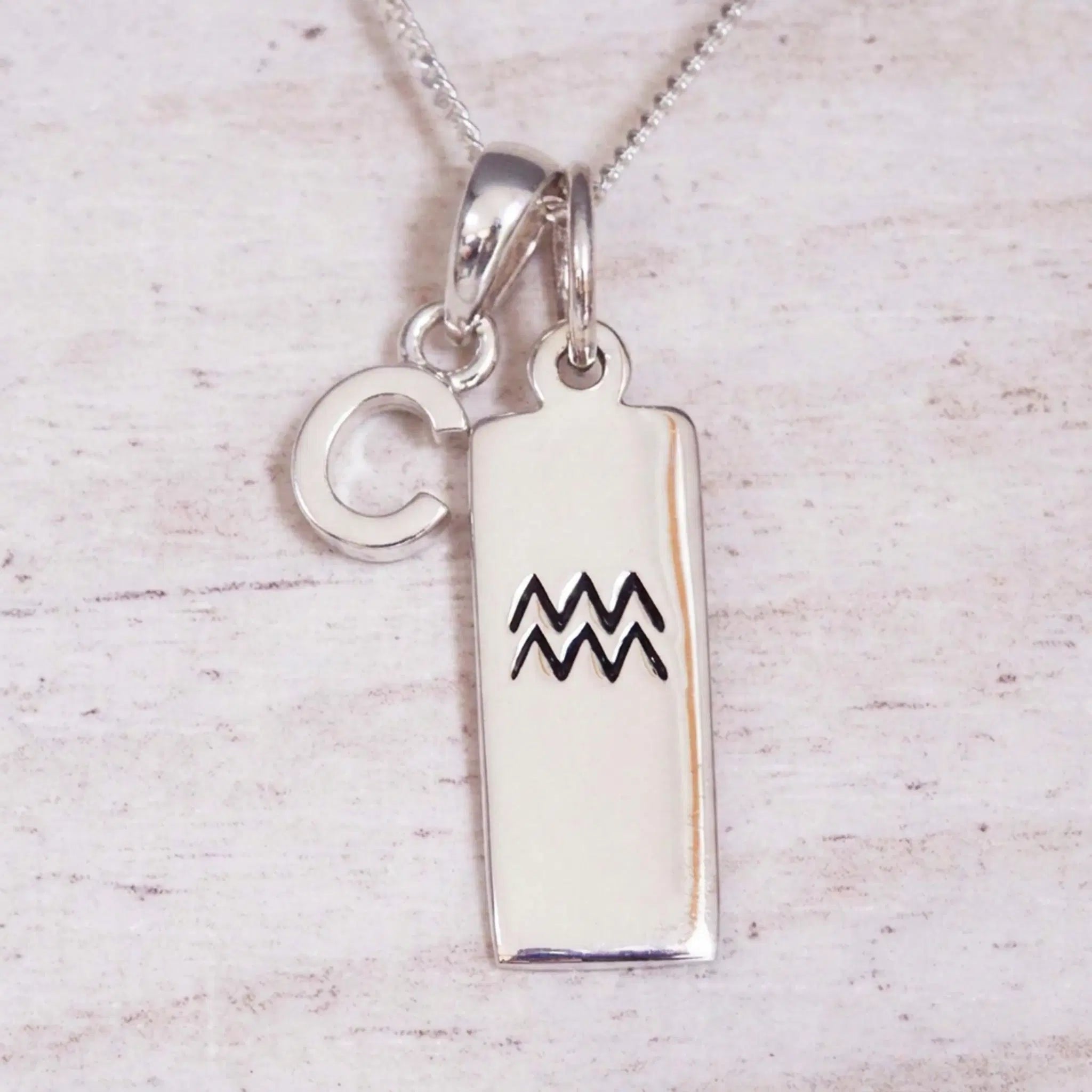 Sterling Silver C Initial and Aquarius Necklace on a fine silver chain against a light wooden background