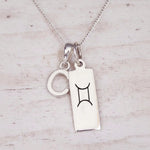Sterling silver Gemini initial necklace with a letter C and engraved zodiac bar on light wood