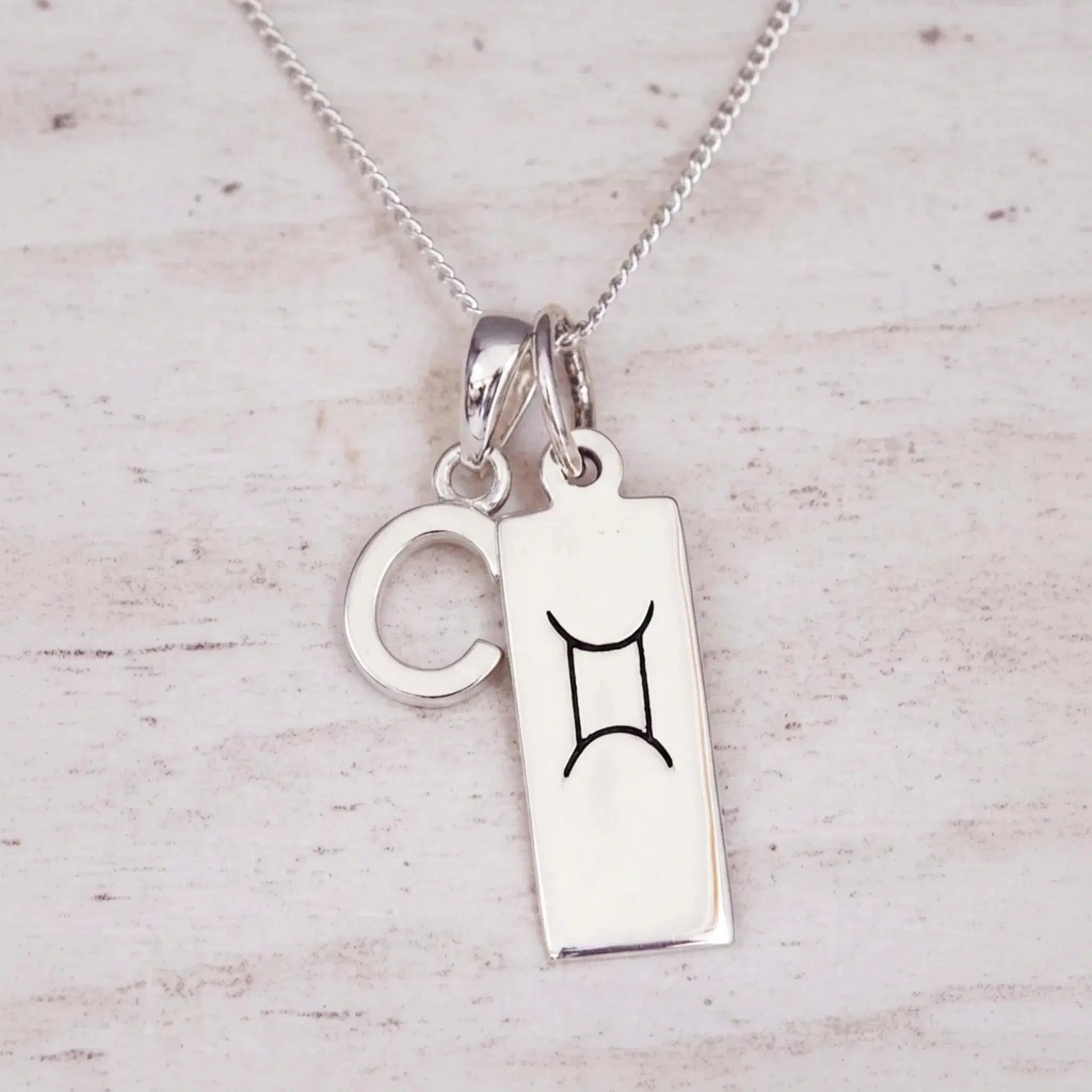 Sterling silver Gemini initial necklace with a letter C and engraved zodiac bar on light wood