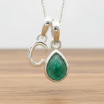 Silver Initial C necklace with a teardrop-shaped Emerald gemstone pendant hanging above a rustic wooden surface