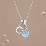 Sterling silver initial C and November natural blue topaz necklace on a taupe background with sparse ivory flowers