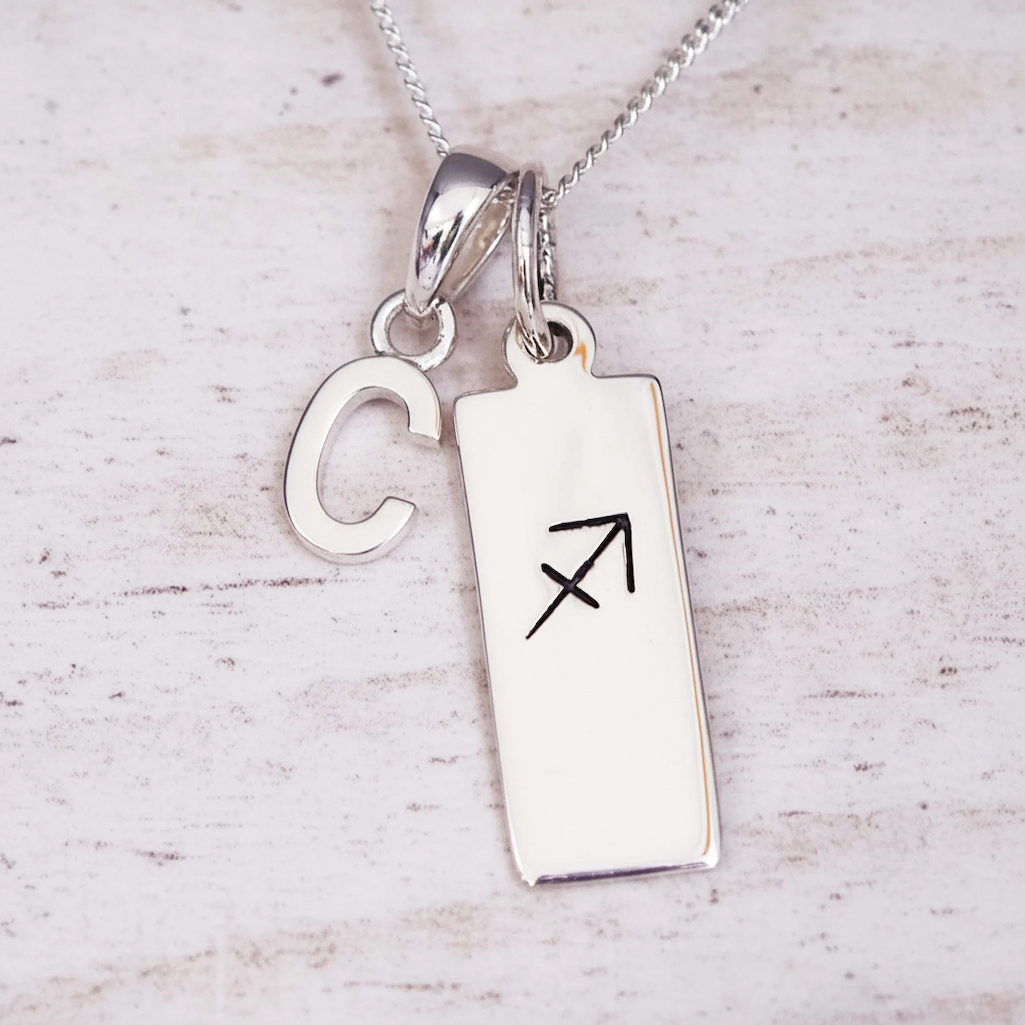 sterling silver necklace with a 'C' initial pendant and a sagittarius zodiac pendant on a light background