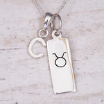 sterling Silver necklace with a 'C' initial pendant and a taurus zodiac star sign pendant on a light wooden background.
