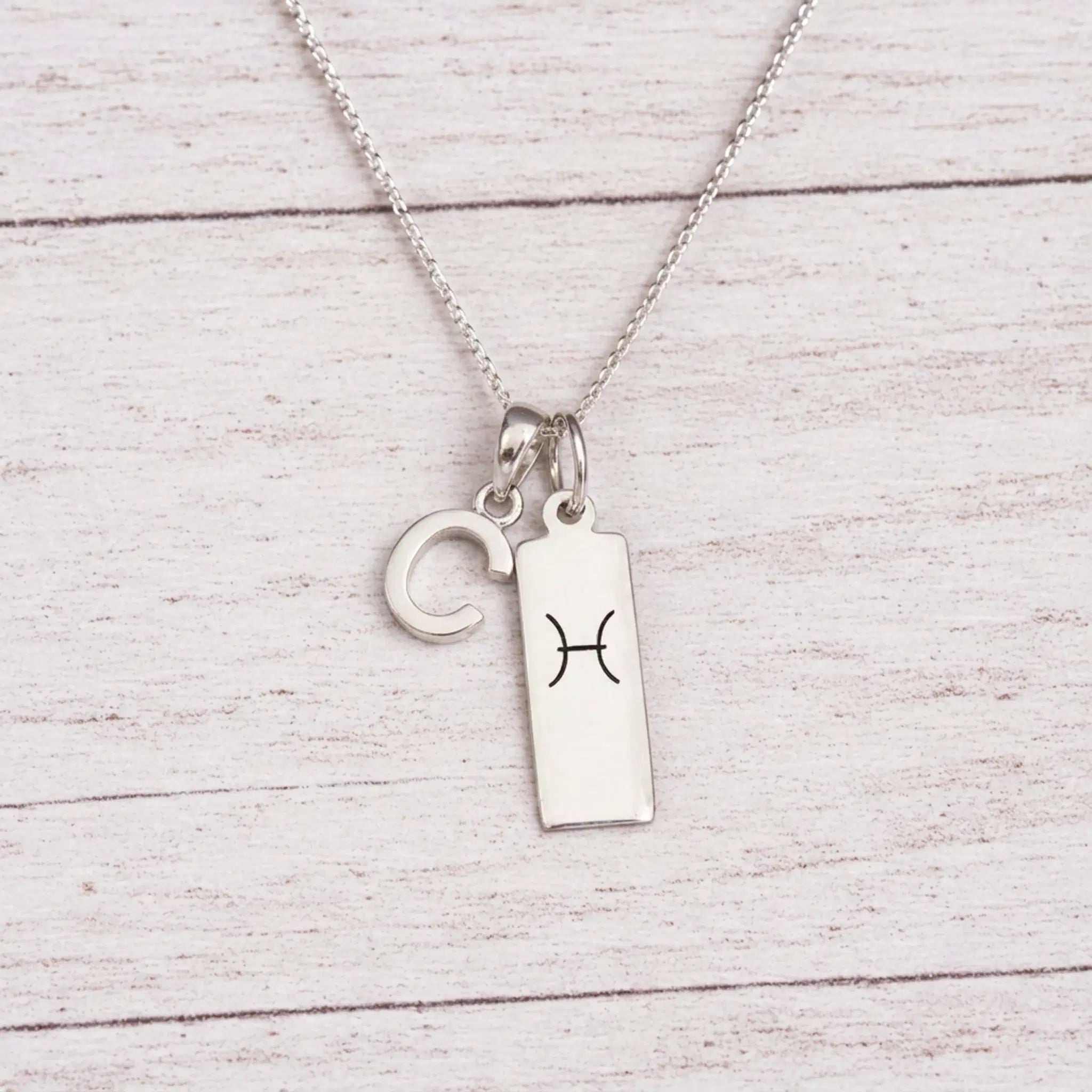 sterling silver C initial Pisces Necklace on a fine silver chain against a light wooden background