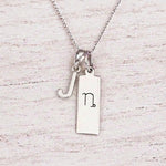 sterling silver J initial Capricorn zodiac sign necklace on a fine silver chain against a light wooden background
