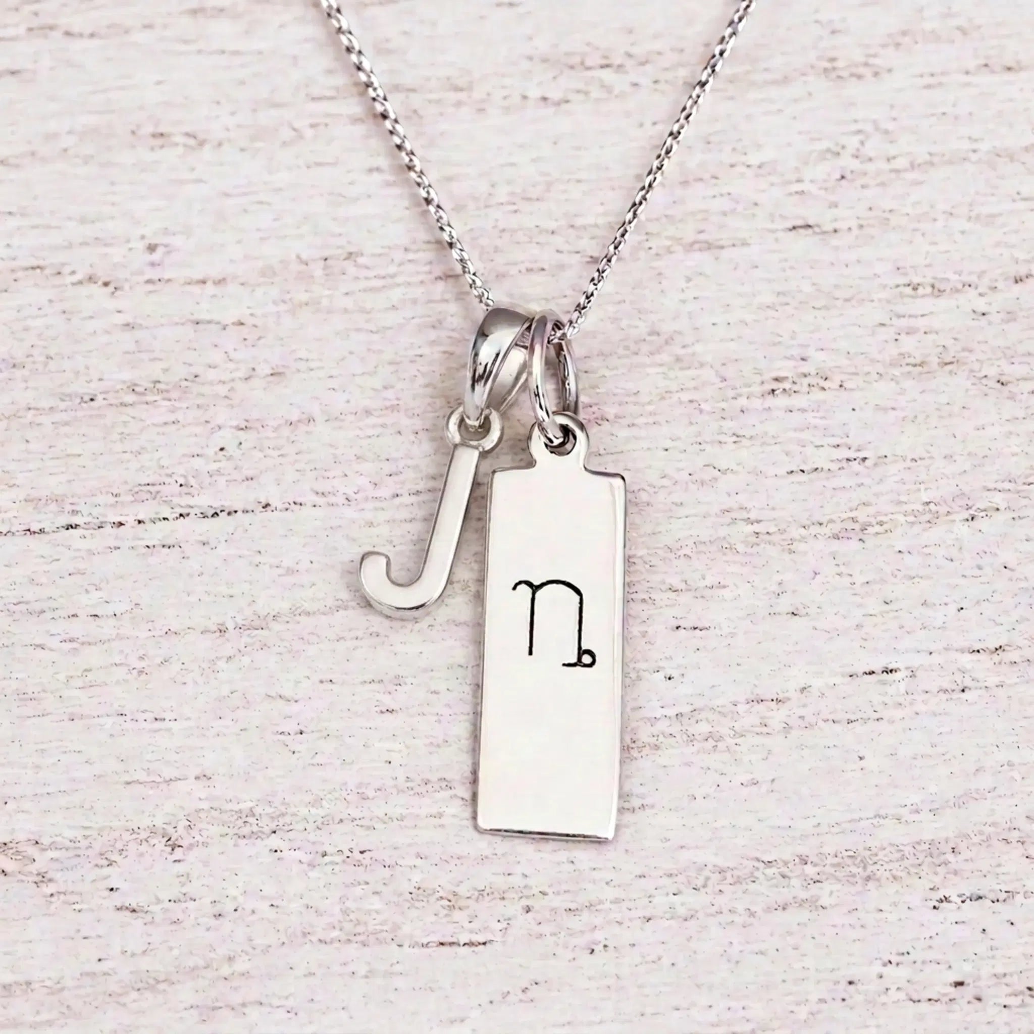 sterling silver J initial Capricorn zodiac sign necklace on a fine silver chain against a light wooden background