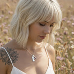 Woman with blonde hair and a tattoo in a field of flowers wearing a silver necklace with garnet 